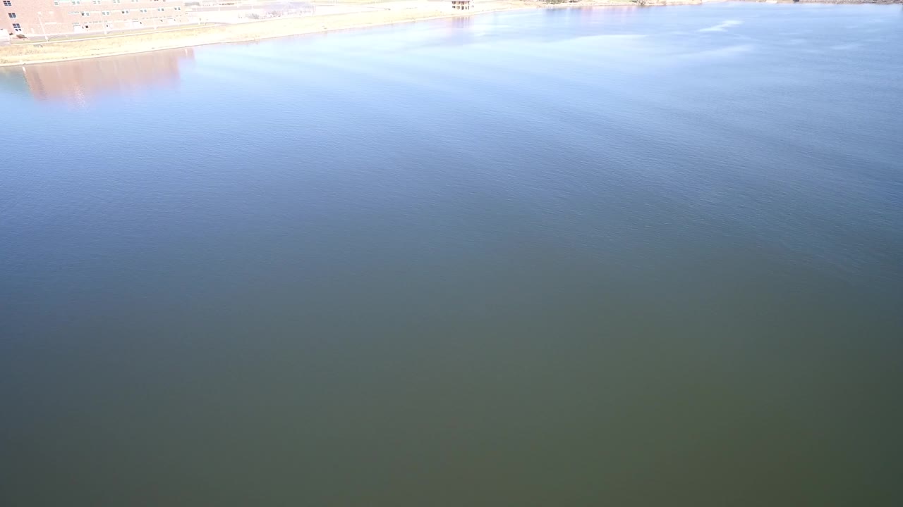 Opening frame of Hidden Lake, Colorado showing broad blue-green water, faint ripples, a pale shoreline strip along the top, and no visible people.
