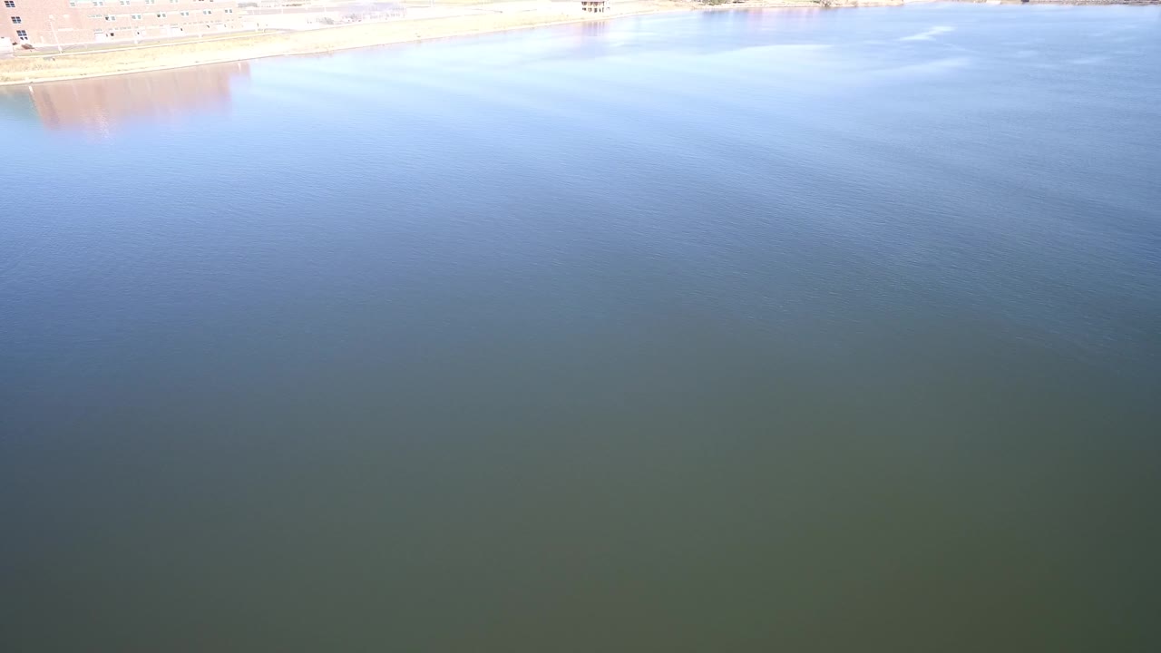 At 0:01, Hidden Lake, Colorado fills the frame with blue water, subtle ripple texture, a thin overexposed shore band, and no visible people.