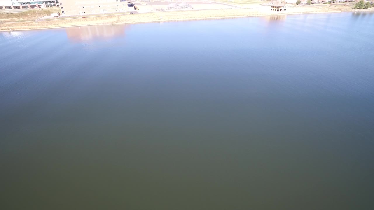 High-angle view over blue green lake water with a bright shoreline at the top edge.