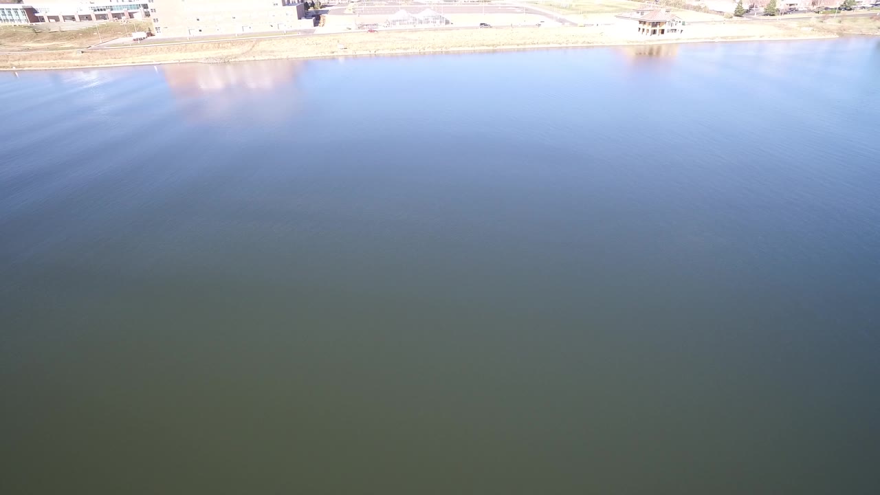 Aerial view over blue-green lake water with shoreline at the top.