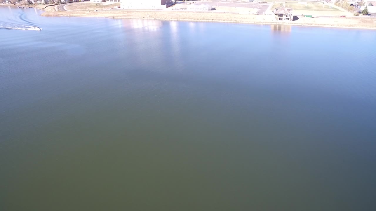Wide aerial view of open lake water below a thin shoreline strip.