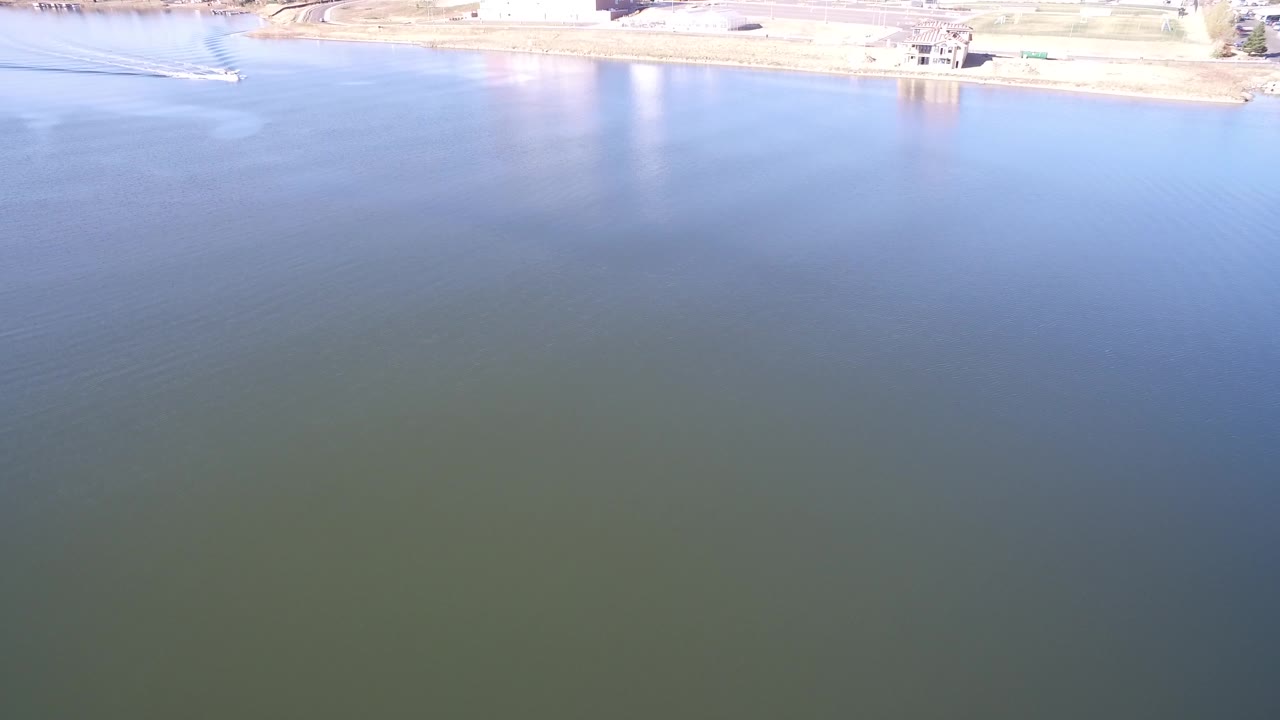 Second frame of Hidden Lake, Colorado showing a wide water surface, pale shoreline, small waterfront structures, and no visible people.