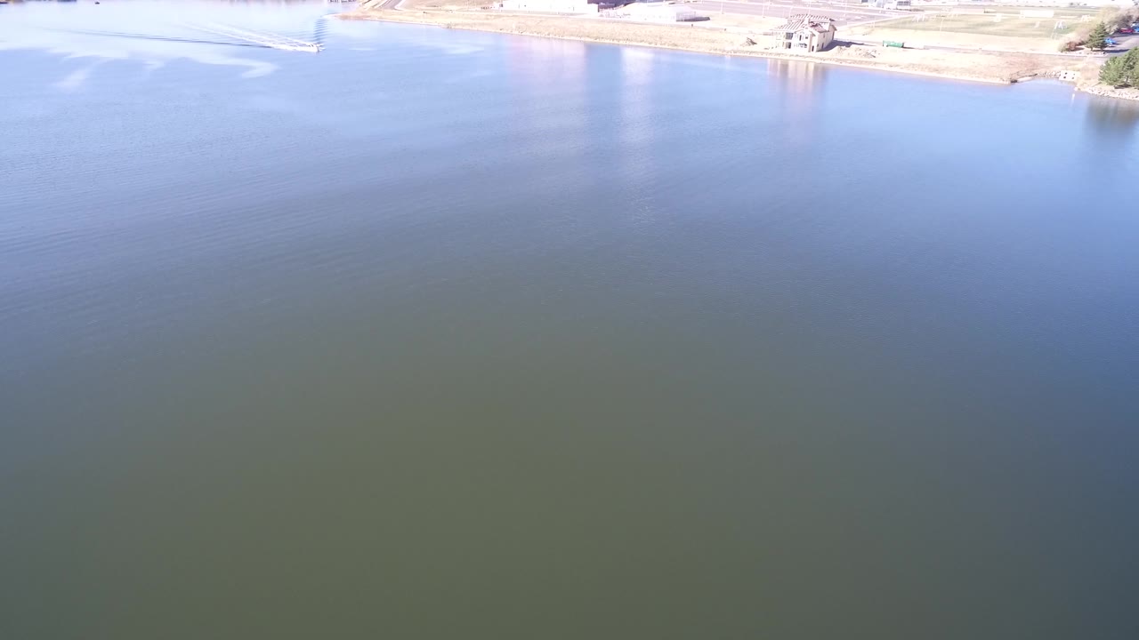 Blue-green lake water seen from above with shoreline and small land forms near the top.