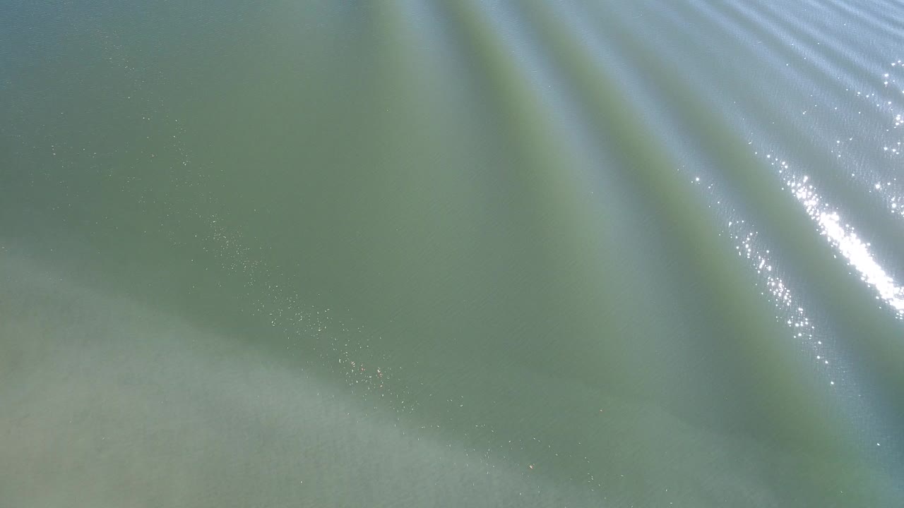 Aerial frame of Hidden Lake water showing pale underwater bands, soft ripples, and no visible people.