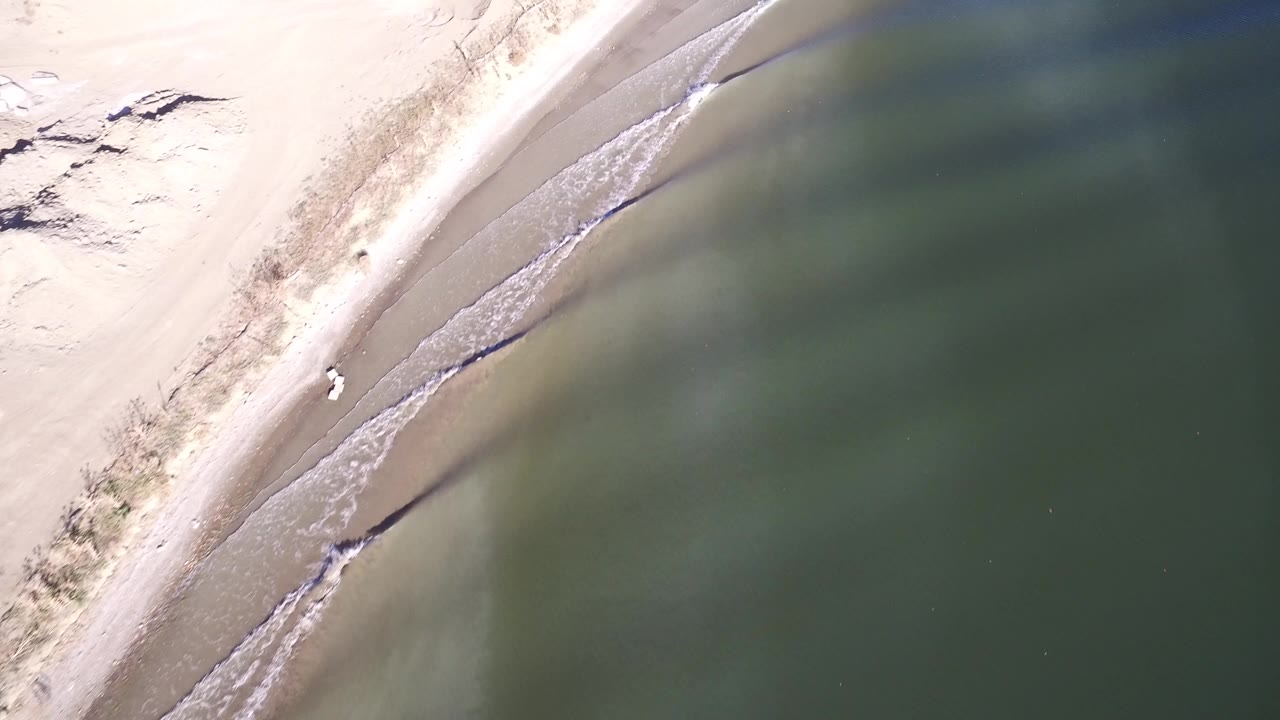 Overhead view of pale sand and green lake water
