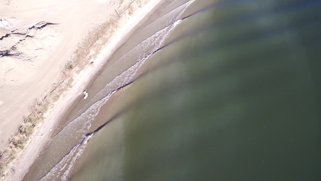 Overhead view at Hidden Lake, Colorado with the sandy beach running diagonally along calm green water and small ripples near the shore.