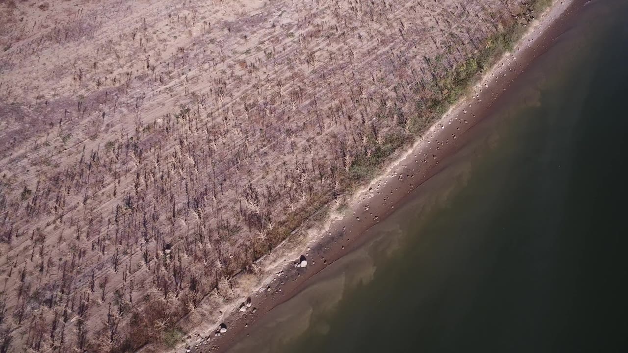 Aerial view in Hidden Lake, Colorado, with pale dry ground, a thin rocky bank, dark water, and no visible people.