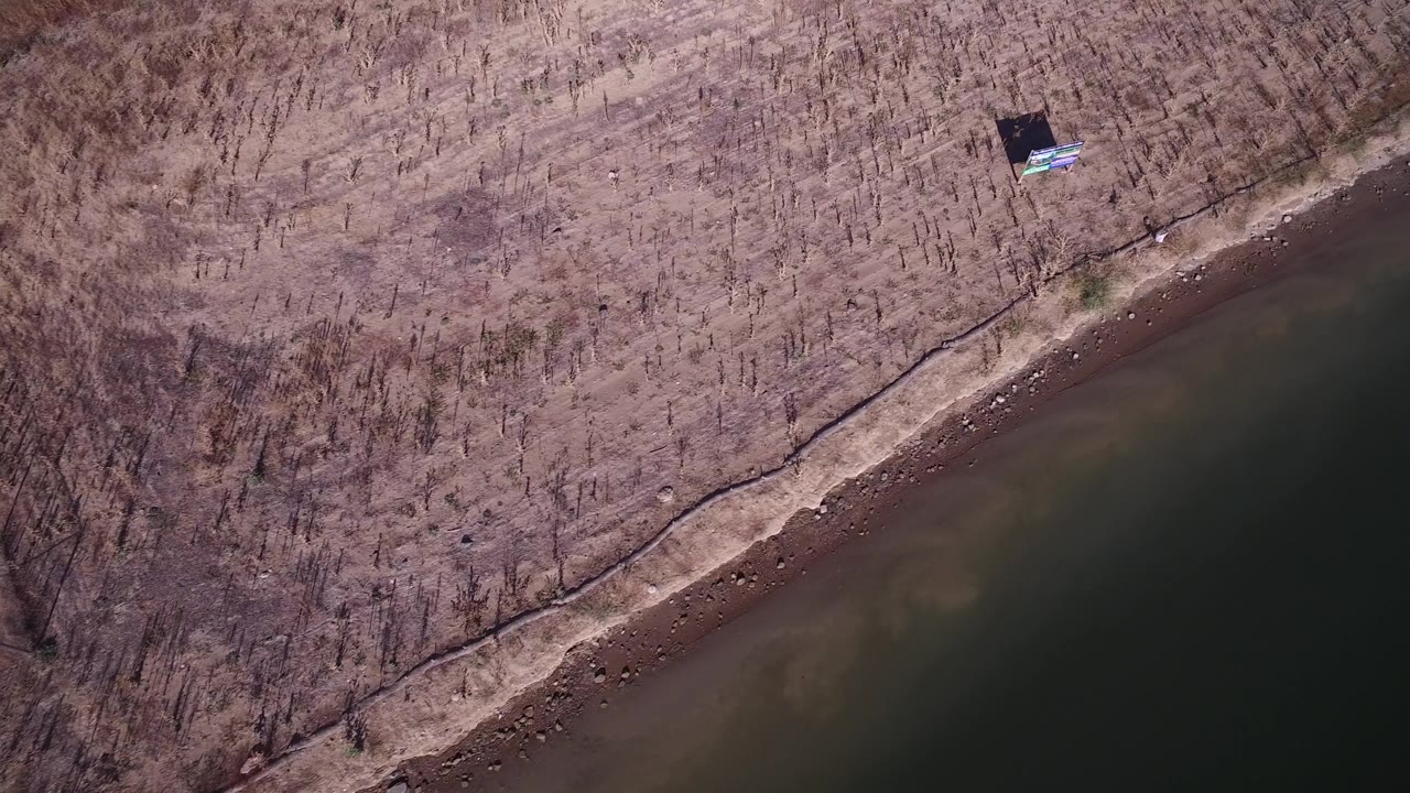 Overhead view of lake water beside a brown shoreline and leafless brush.