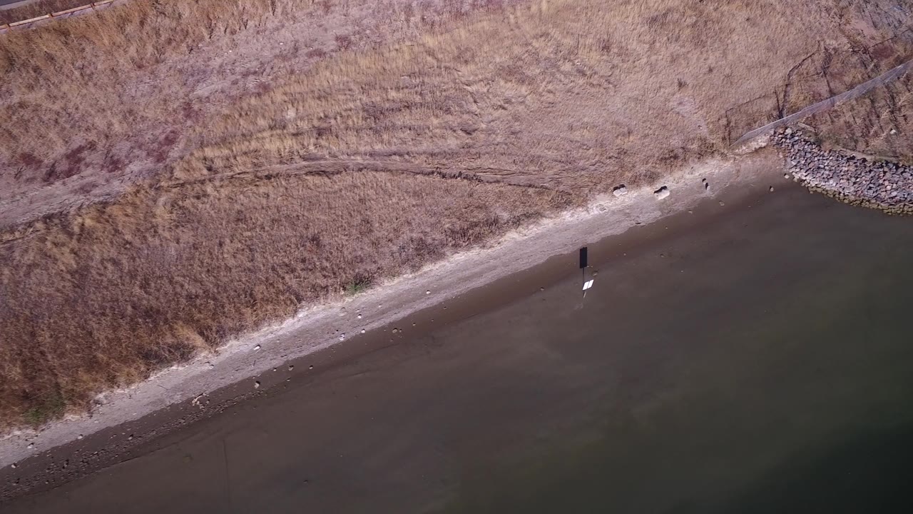 Aerial view of Hidden Lake, Colorado with the beach running diagonally between dark water and dry grass, including scattered stones and no visible people.