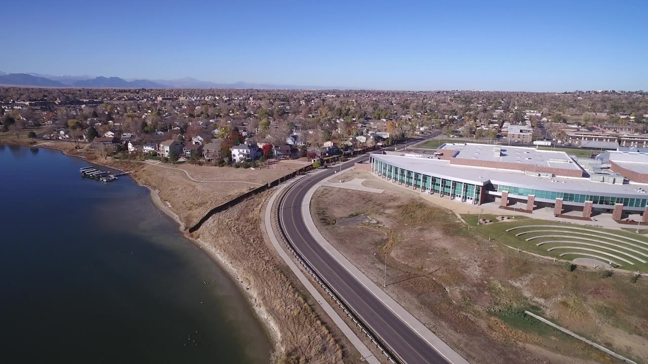 Aerial view of a lake beside a curving road and large waterfront building.