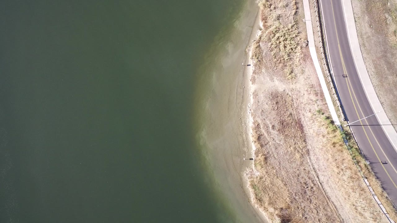 Overhead view of green water, sandy shore, and a curving road.