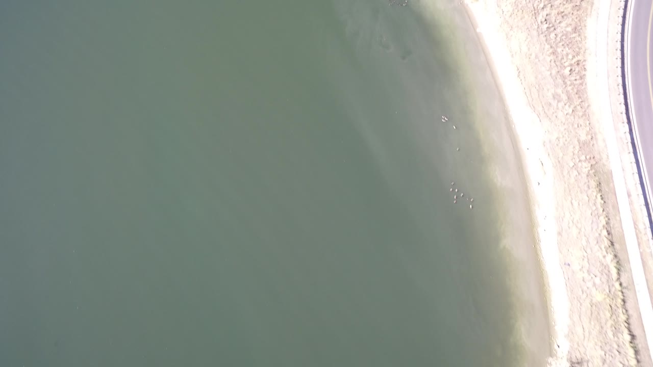 Aerial frame over Hidden Lake, Colorado showing green water, a thin pale beach, bright exposed sand, and no visible people.