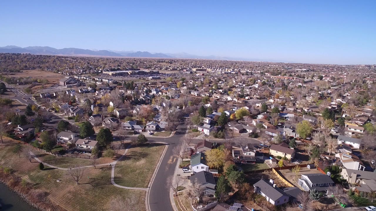 A high aerial view in Hidden Lake, Colorado shows clustered rooftops, open lawns, bare trees, yellow foliage, a wide blue sky, and no visible people.