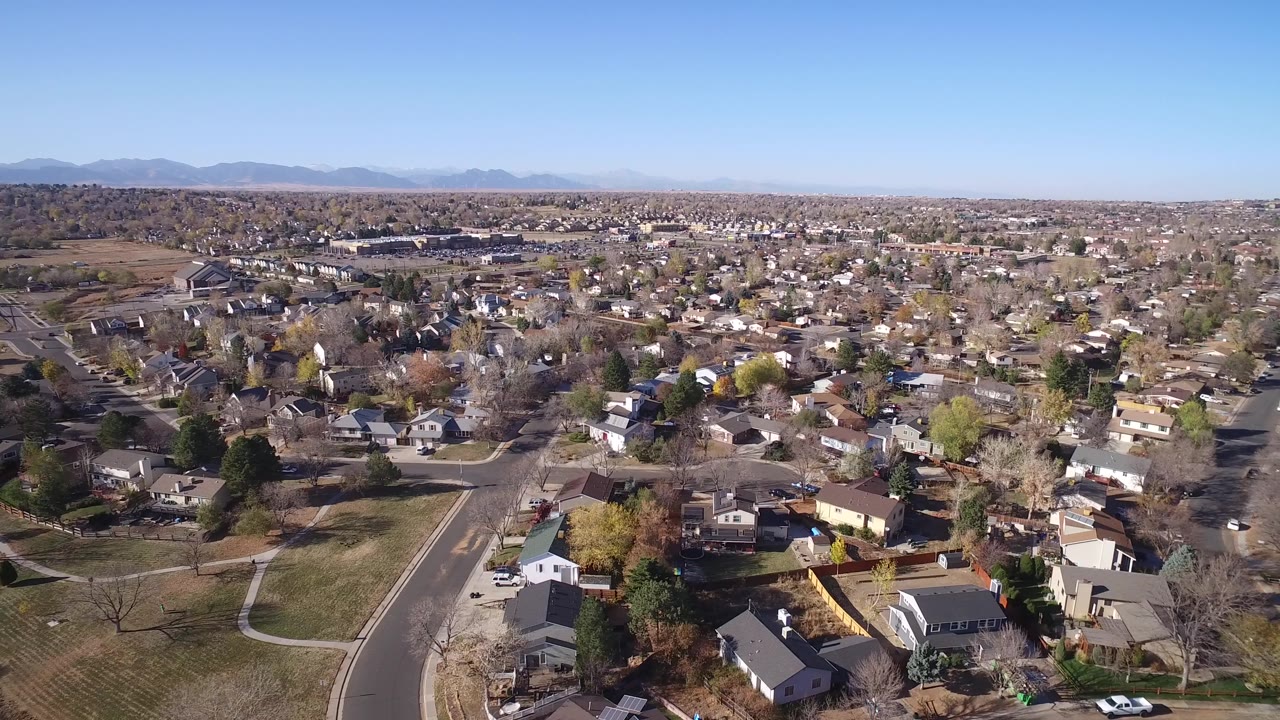 Suburban grid with houses, tree cover, open lawns, and a mountain horizon.