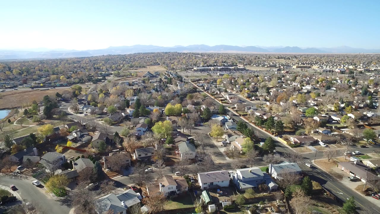 Aerial view over suburban houses, streets, trees, water, and distant mountains.