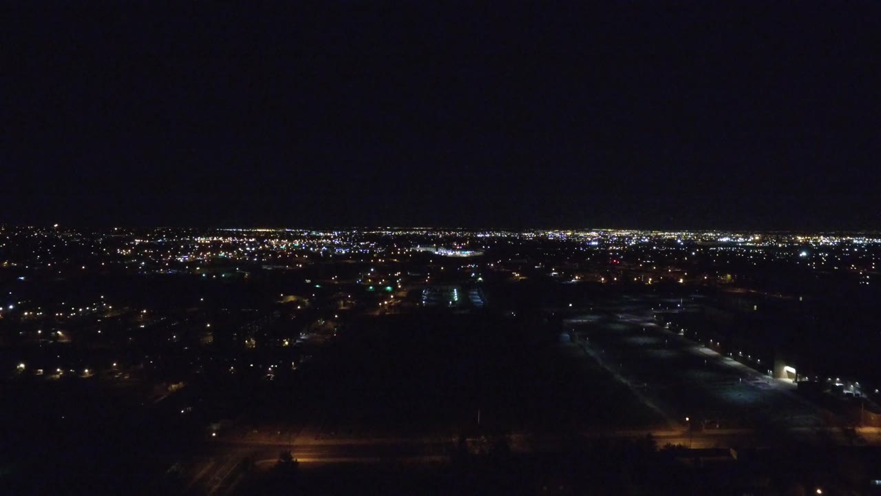 Denver at night from an elevated view, with a low horizon of bright city lights above dark foreground blocks and no visible people.