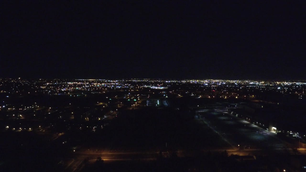 Denver city lights stretch across the horizon while dark lots and scattered road lights fill the lower frame, with no visible people.