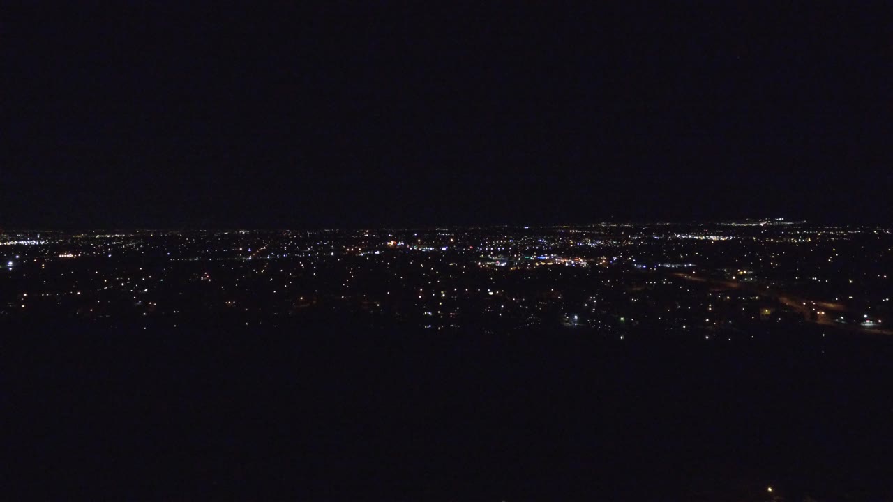 A dark aerial view over Denver, Colorado shows a thin horizon of distant city lights with a black foreground and no visible people.