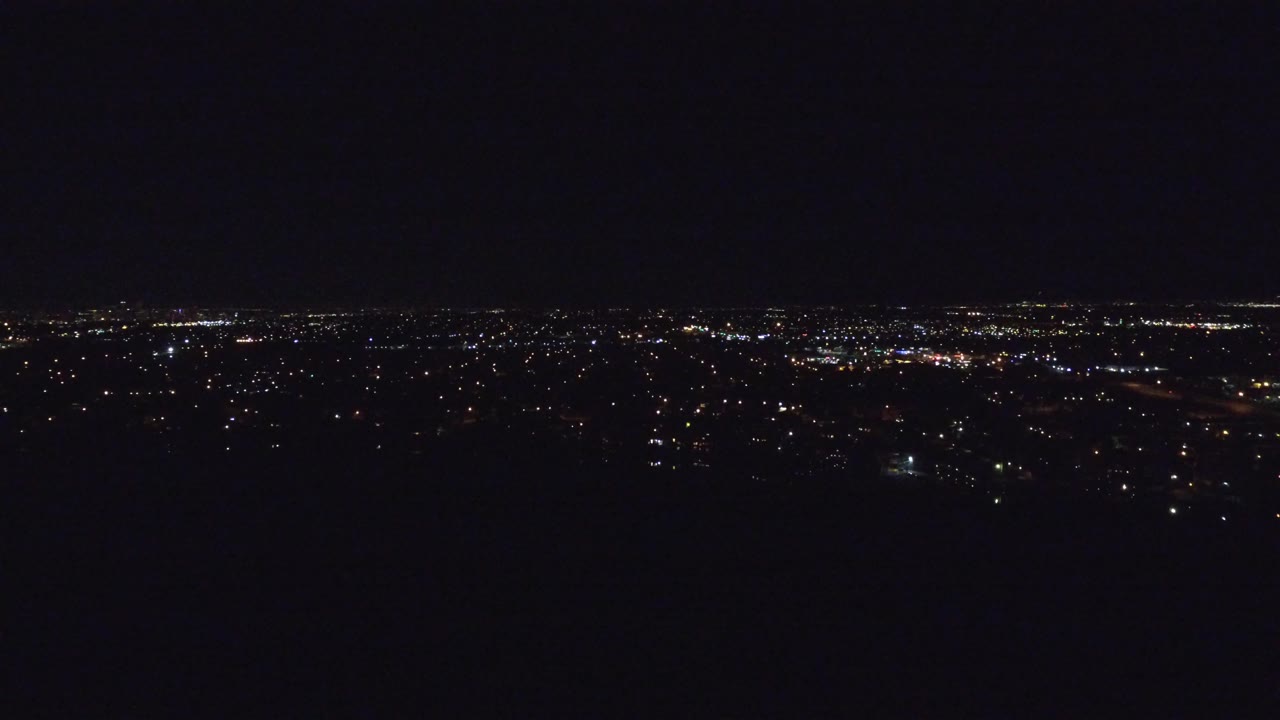 Wide night aerial with distant city lights across a dark horizon.