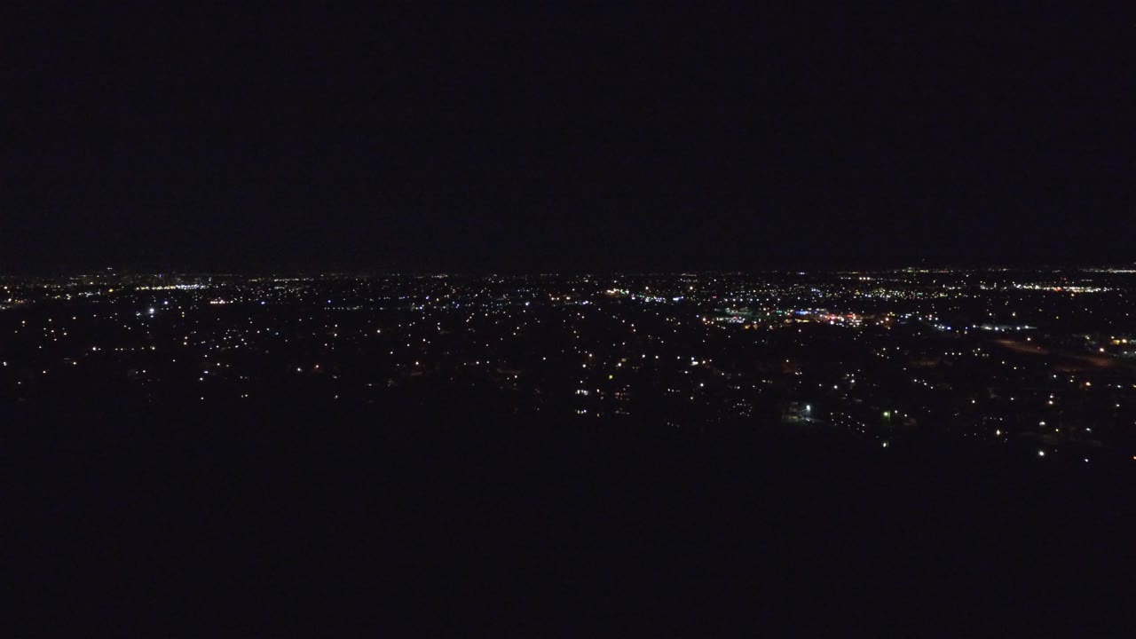 Denver night aerial frame with a broad band of small white and amber lights set low against a large black sky, with no visible people.