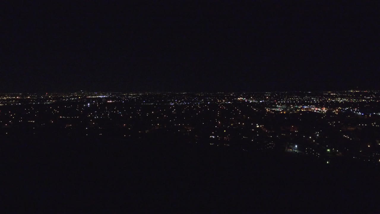 A high nighttime view of Denver, Colorado, showing a broad band of small city lights with a darker foreground and no visible people.
