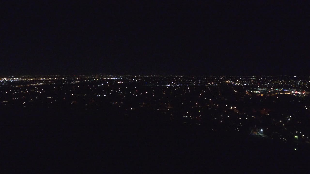Wide night view over Denver, Colorado, with scattered city lights along a low horizon, a mostly black foreground, and no visible people.