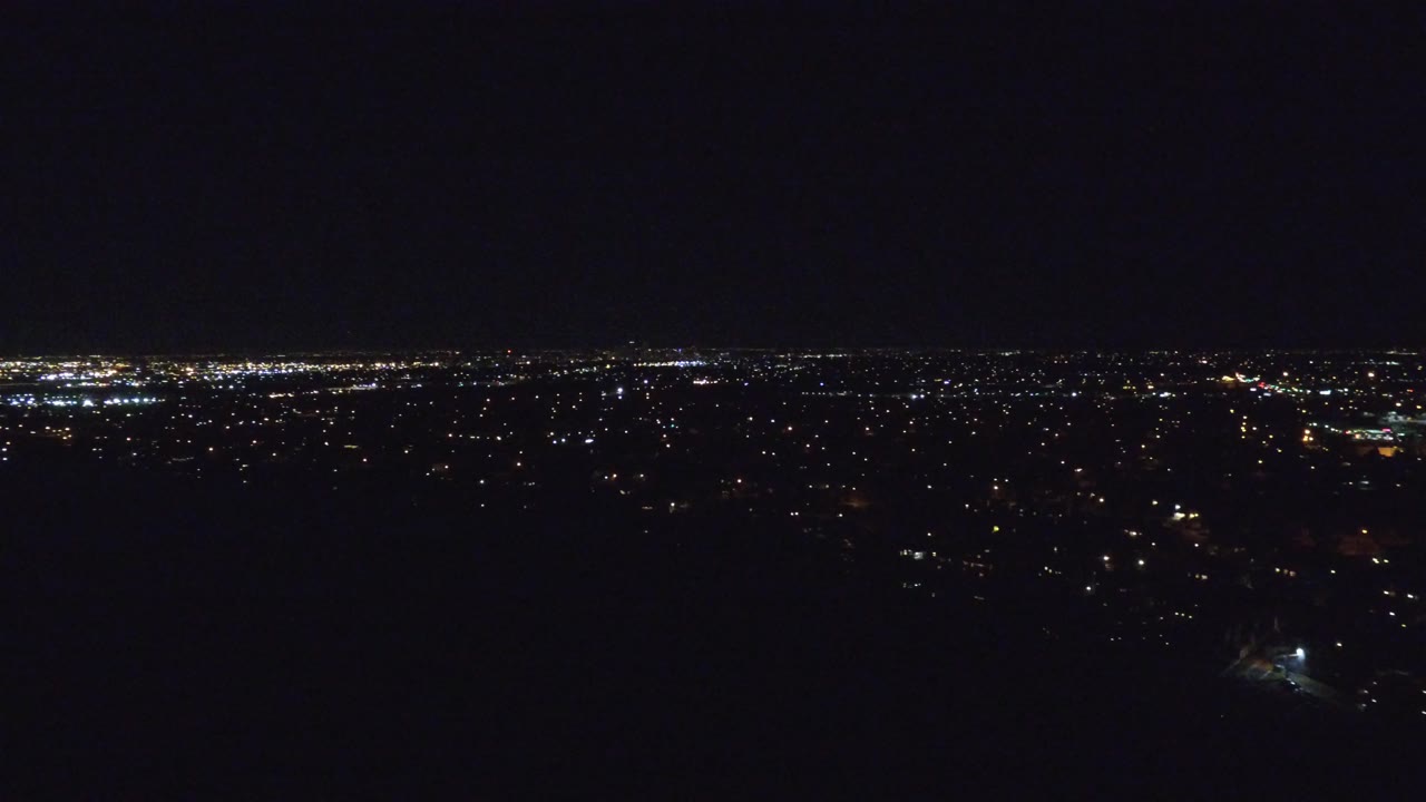 Wide dark nighttime city view with distant lights along the horizon.