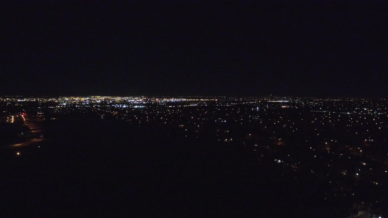 Elevated nighttime Denver view with a bright band of distant lights near the horizon and darker residential lights below, with no visible people.