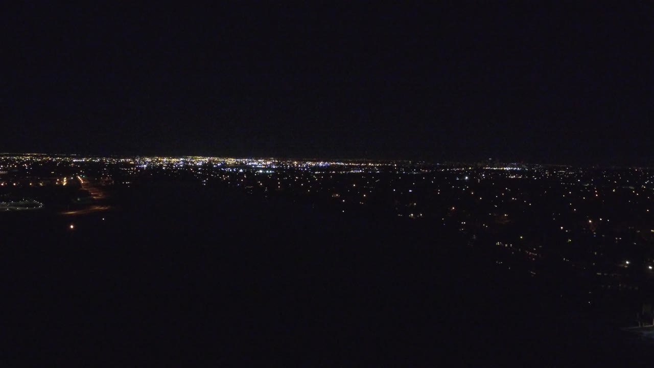 Denver city lights stretch across the horizon at 0:01, with dark land in the foreground and no visible people.