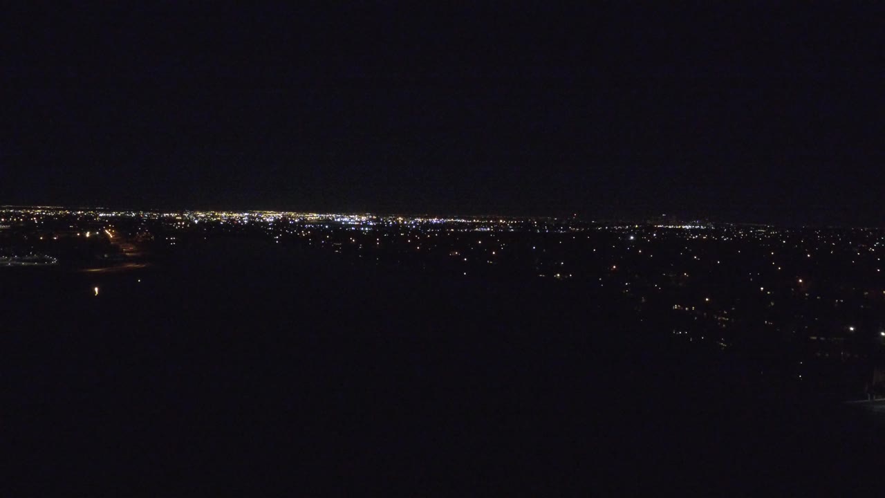 Denver at night with a broad black sky, dark foreground, and a thin band of distant city lights across the horizon, no visible people.