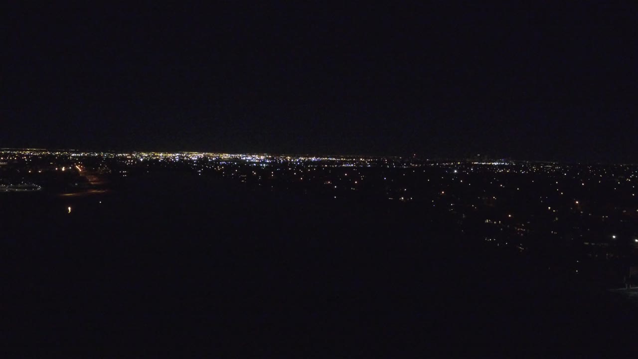 A wide Denver night view shows scattered white and yellow lights along a low horizon with a nearly black foreground, no visible people.