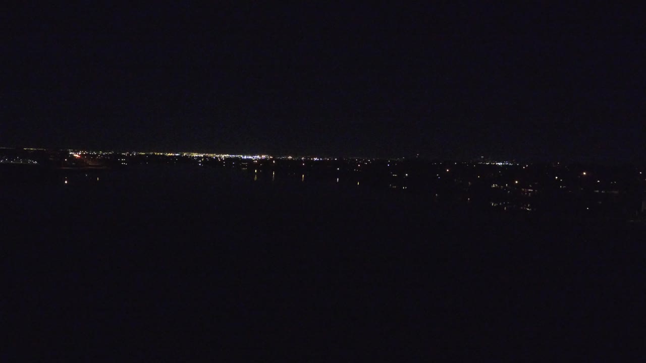 A dark nighttime aerial view over Denver, Colorado, with a thin line of distant city lights near the horizon and no visible people.