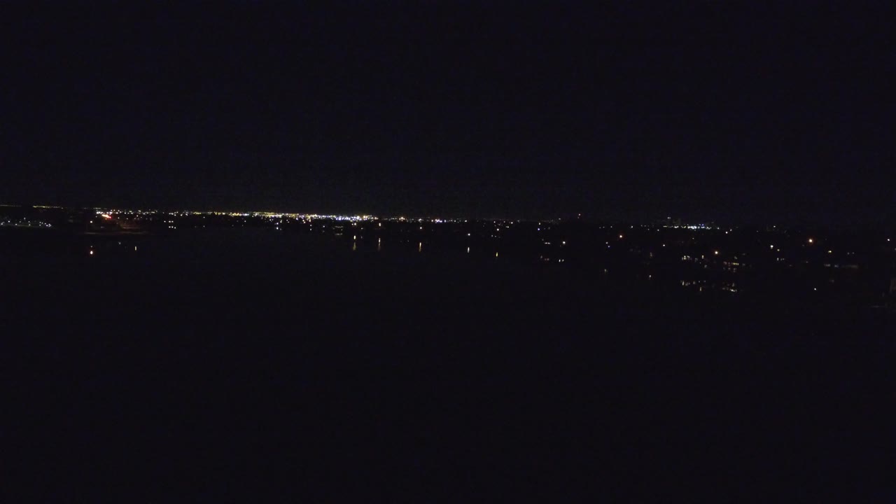 A wide Denver night view shows clustered urban lights stretching across the horizon, with the frame dominated by dark sky and no visible people.