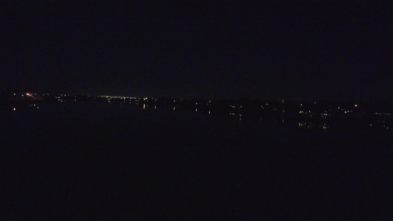 Opening frame of a dark Denver lake at night, with a thin band of distant city lights near the horizon and no visible people.