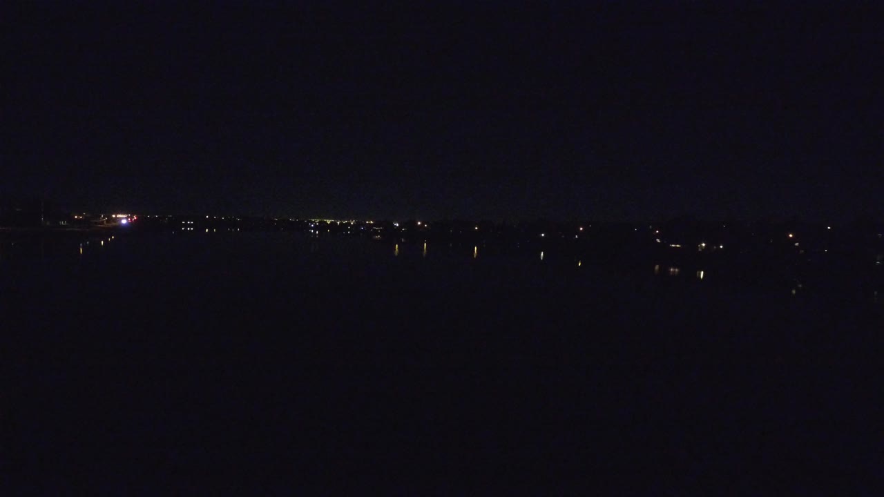 Opening frame of dark water in Denver with a low line of distant lights on the horizon and no visible people.