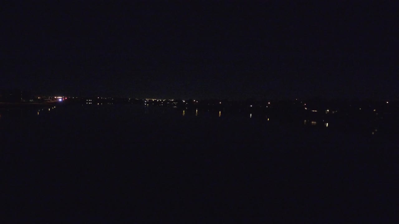 Faint building lights across a dark water surface at night.