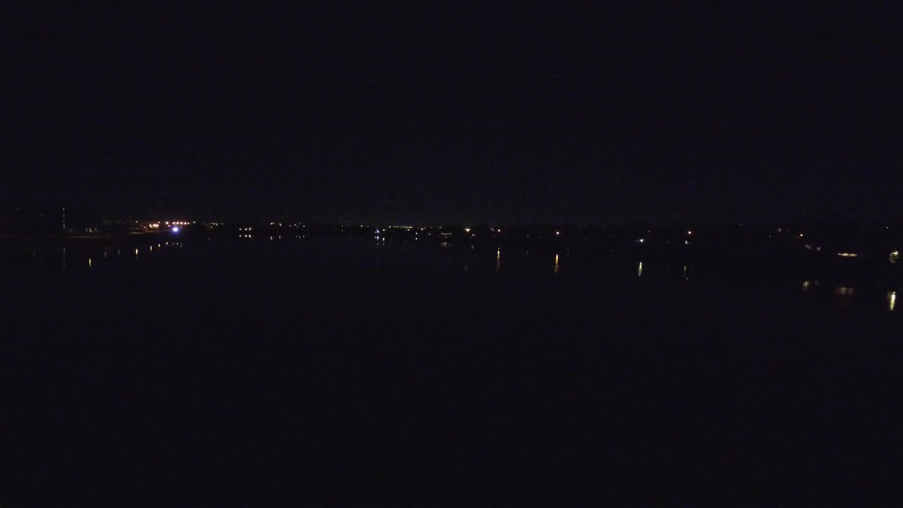 A dark Denver night waterfront frame with a thin band of distant lights near the horizon and dim vertical reflections on the lake, no visible people.