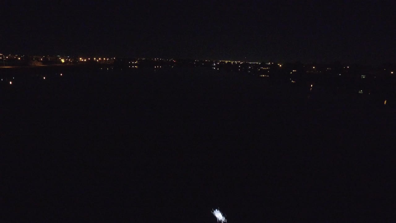 Wide dark nighttime view in Denver, Colorado with distant shoreline lights across the horizon, a small bright vessel light on the river, and no visible people.