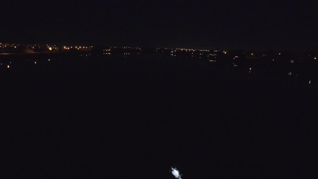The vessel light appears farther across the dark river in Denver, Colorado, with scattered urban lights along the low horizon and no visible people.