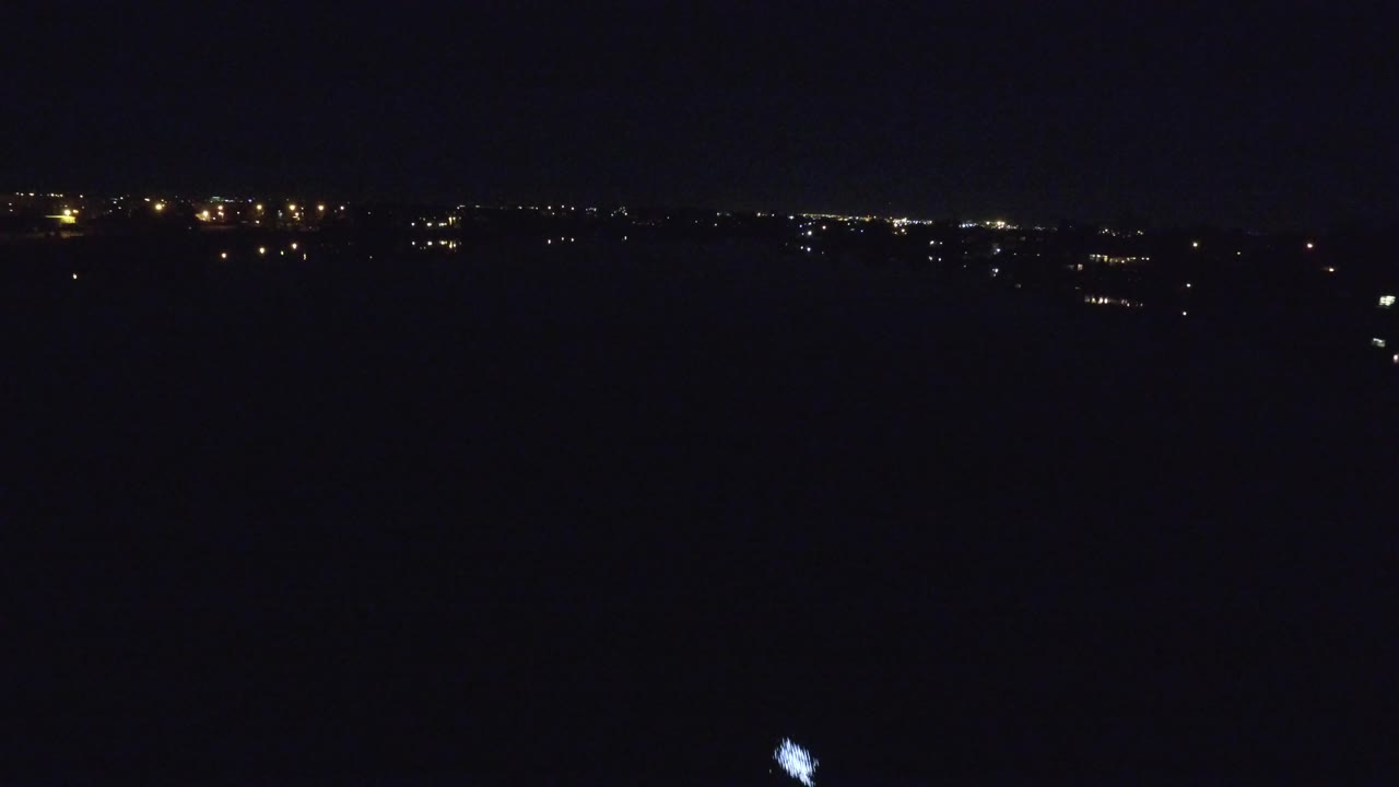 Denver night water scene with the small bright water light nearer the center and a thin band of distant lights across the horizon, no visible people.