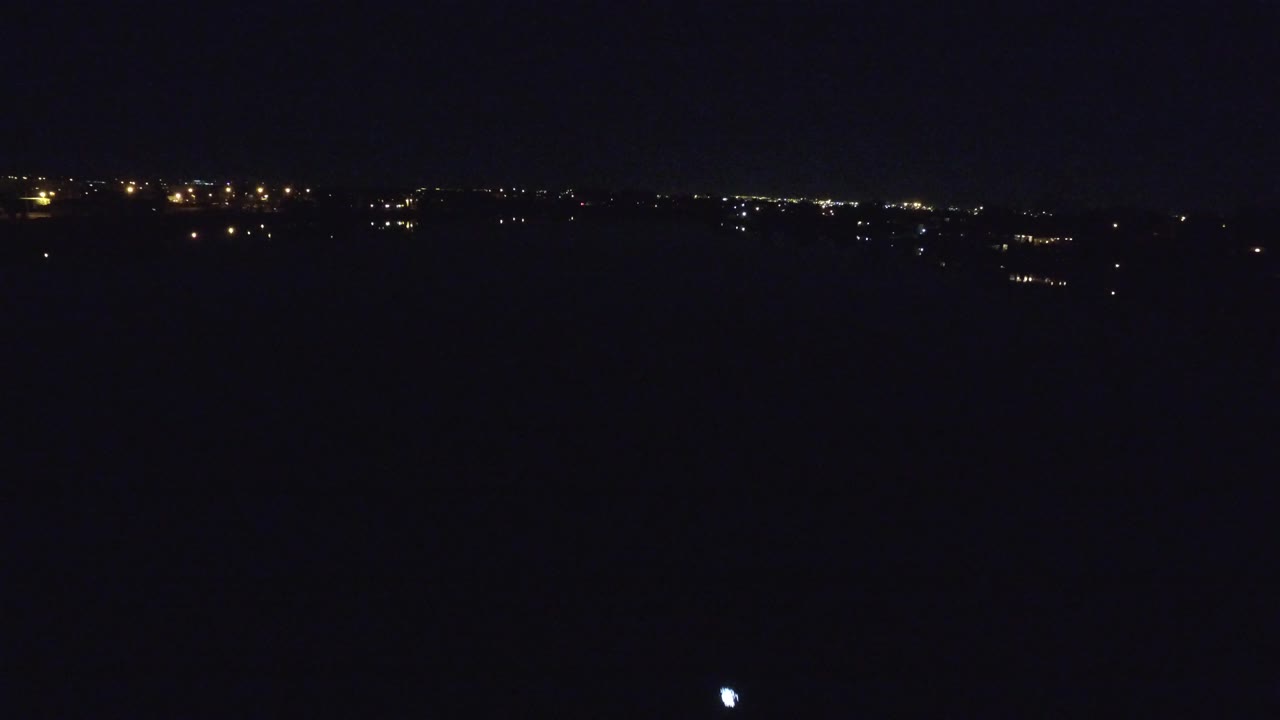 Distant lights along the horizon with a small light on the dark water.