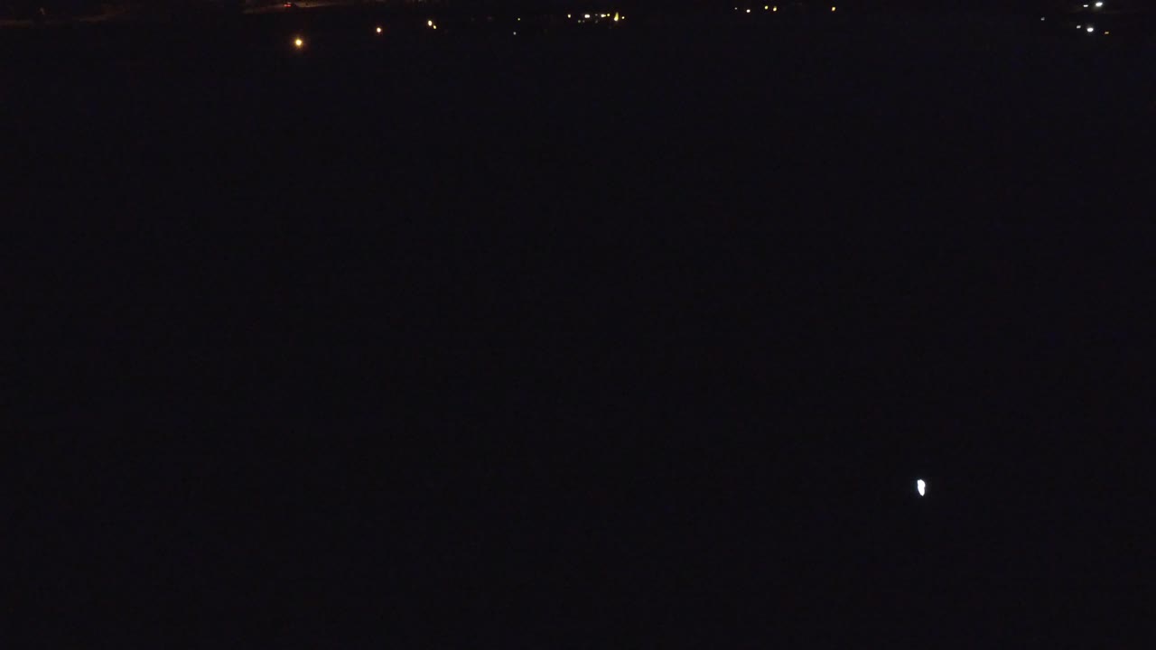 A sparse Denver, Colorado night view contains scattered tiny lights near the lower edge and a nearly black field, with no visible people.