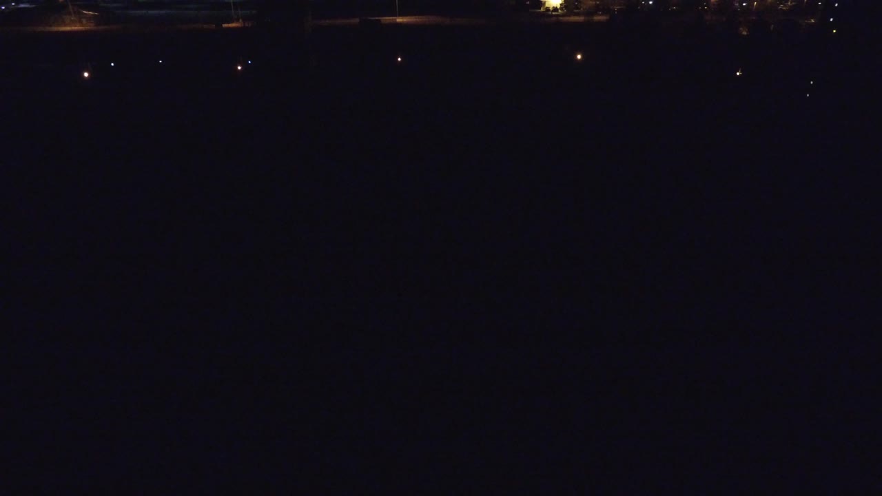 Denver, Colorado night frame showing mostly black water or sky with small warm lights scattered along the far waterfront and no visible people.