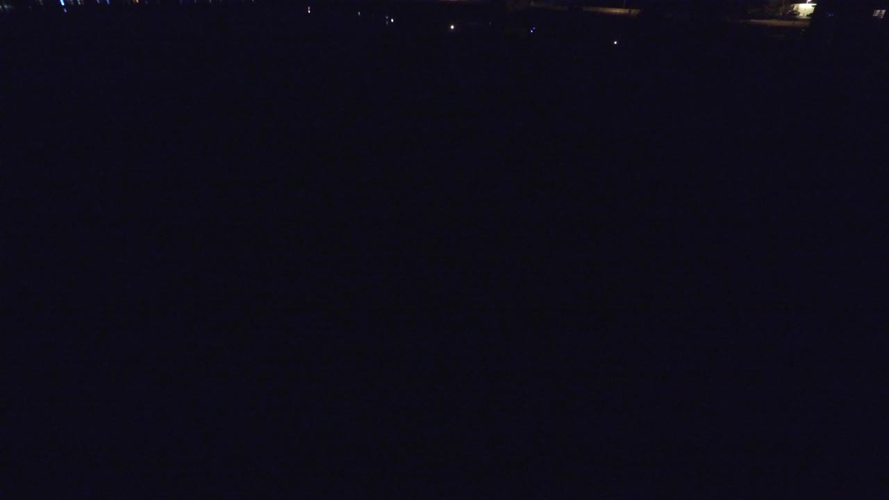Second frame of the Denver night aerial, showing a wide black view with a thin band of small lights near the horizon and no visible people.