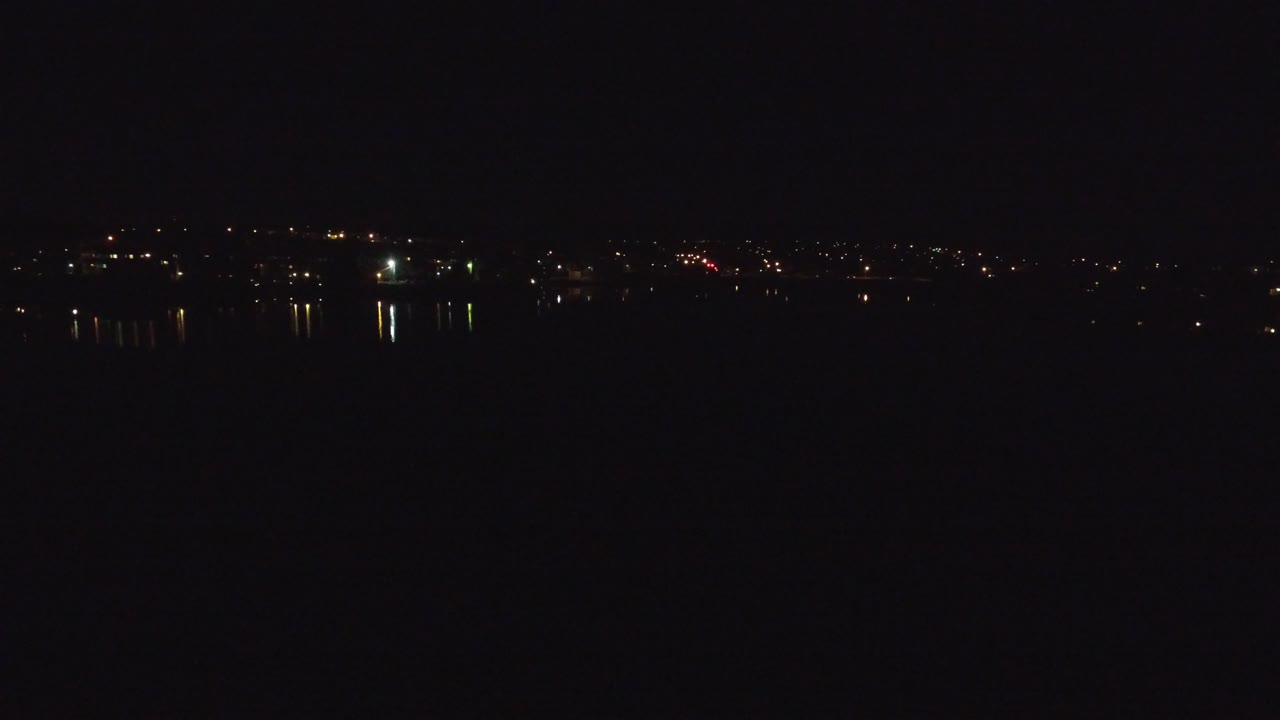 A similar Denver, Colorado night view shows bright white and yellow shoreline lights with small red points and short reflections across the dark water, no visible people.