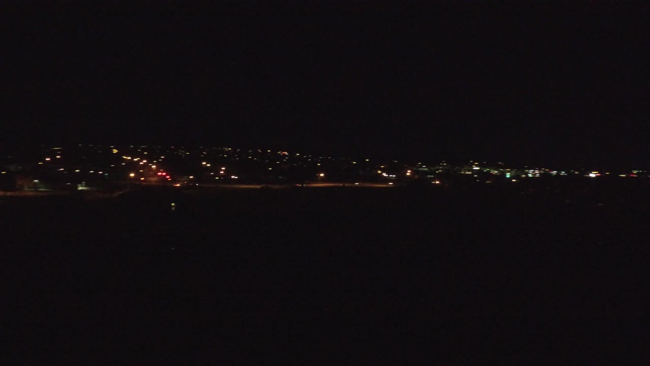 Opening frame of Denver at night with a thin band of distant city lights across the horizon, dark foreground, black sky, and no visible people.