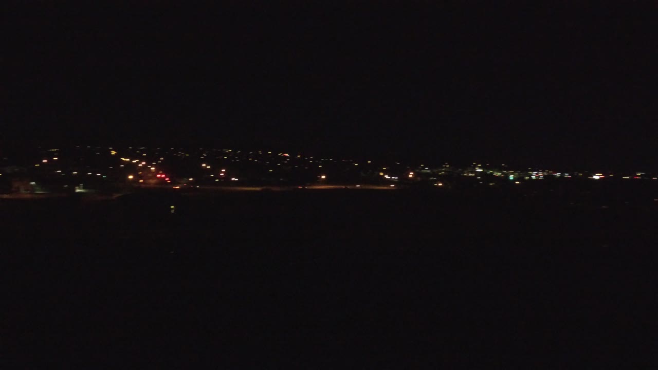 Denver nighttime aerial frame with scattered white and amber lights along the horizon, a dark open foreground, and no visible people.