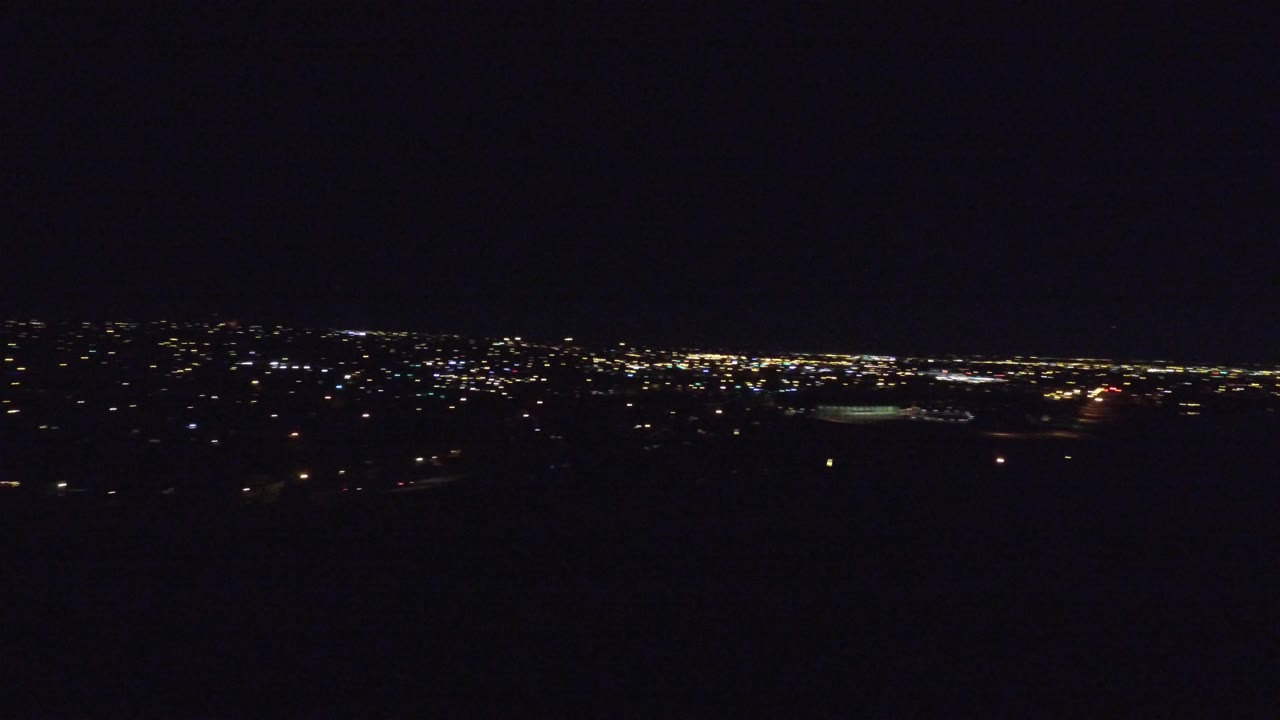 Opening frame of Denver at night from an elevated view, with scattered city lights along the horizon, a dark foreground, and no visible people.