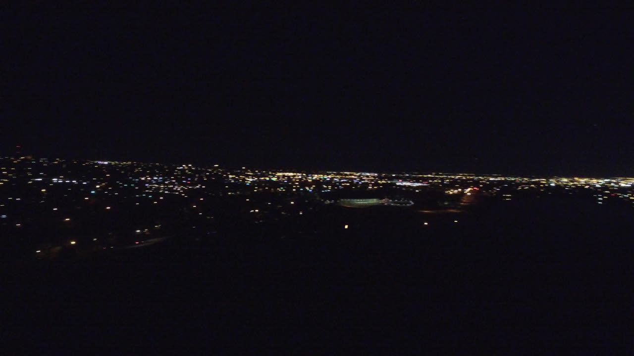 Wide night view of city lights and a faint lit oval area.