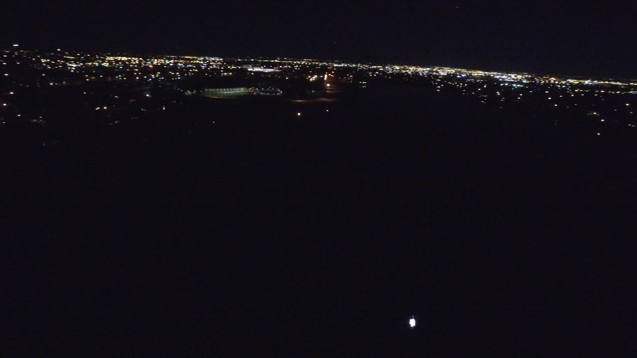 Denver, Colorado at night from an aerial viewpoint, with a thin band of city lights across the upper frame and no visible people.